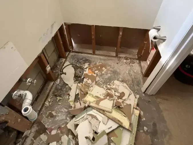 Wallboard fragments cover the bathroom floor below sections of exposed wooden framing