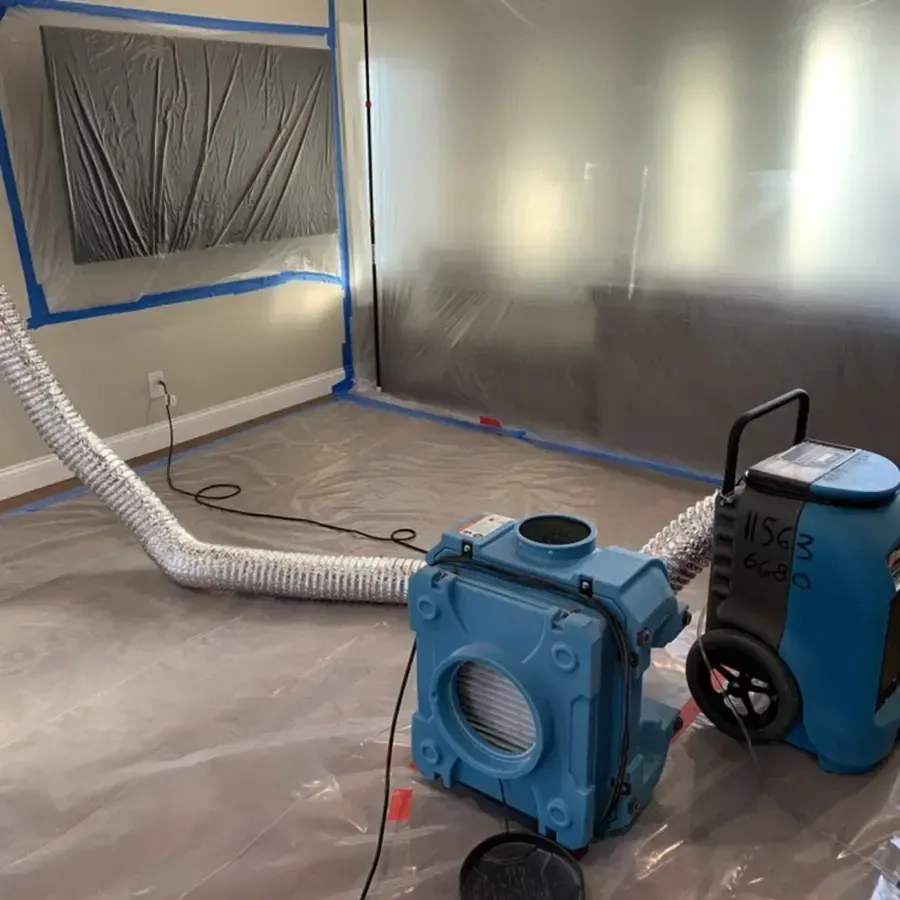 A dehumidifier operating behind plastic containment during an interior water damage dry-out
