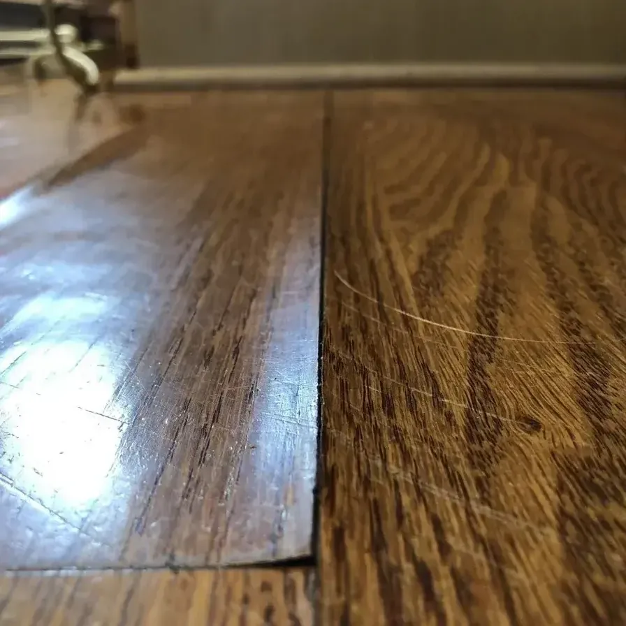 Hardwood boards rise along a damaged seam where water has affected the floor