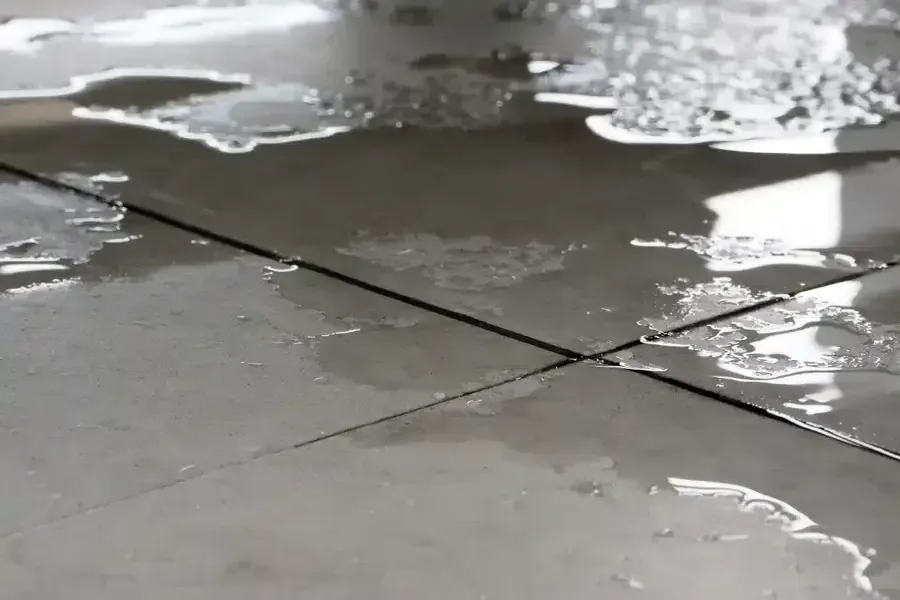 Water pooled across square floor tiles with light reflected on the wet surface