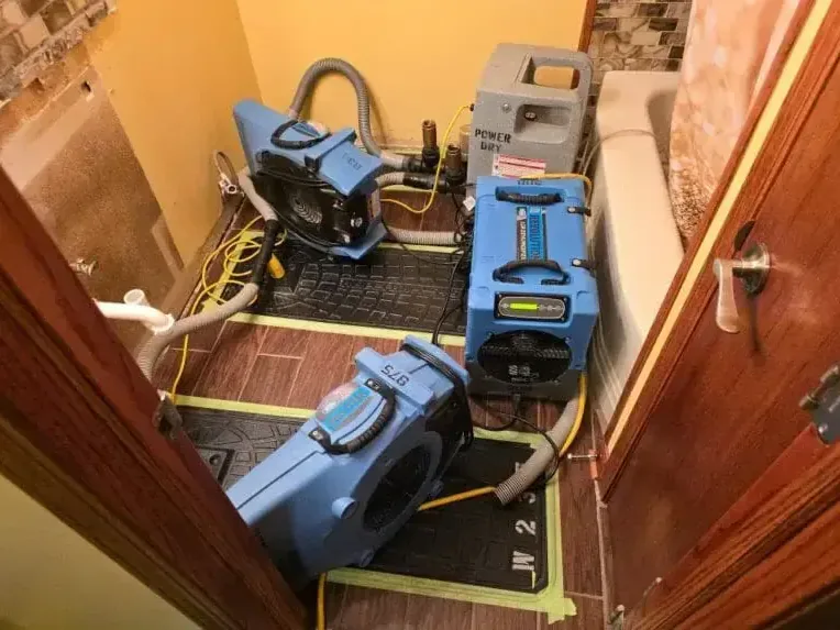 Air movers and dehumidifiers drying walls and flooring in a small room